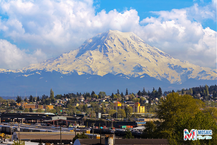 A breathtaking view of Mount Rainier with the city of Tacoma, WA in the foreground, showcasing a mix of urban and natural beauty. This scenic landscape highlights the appeal of living in Tacoma WA, with access to stunning mountain views and vibrant neighborhoods. The Mosaic Real Estate logo is present, emphasizing the professional service provided by Ruthy Taylor, a dedicated Tacoma WA Realtor.